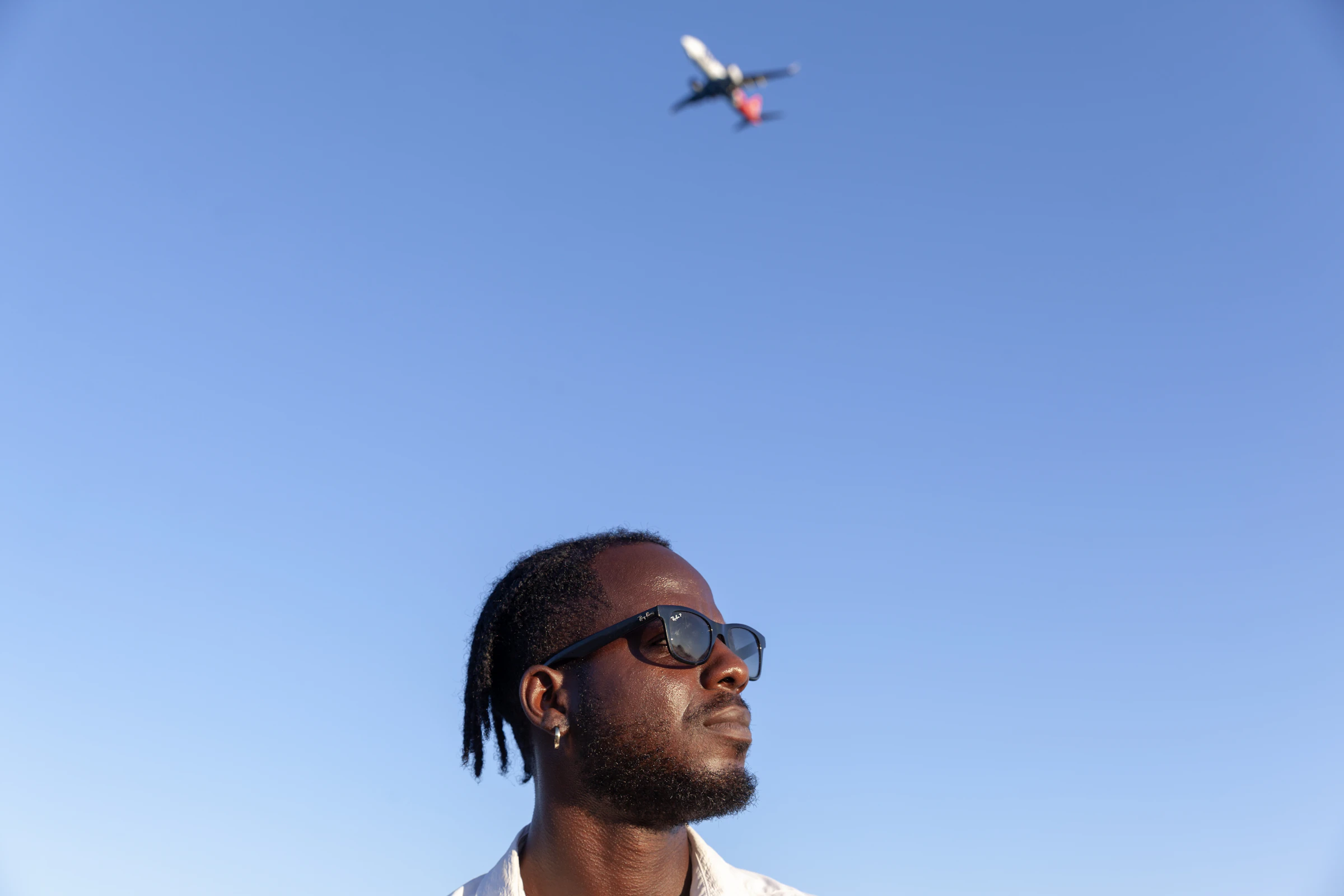 A man in sunglasses looking up as a plane passes overhead